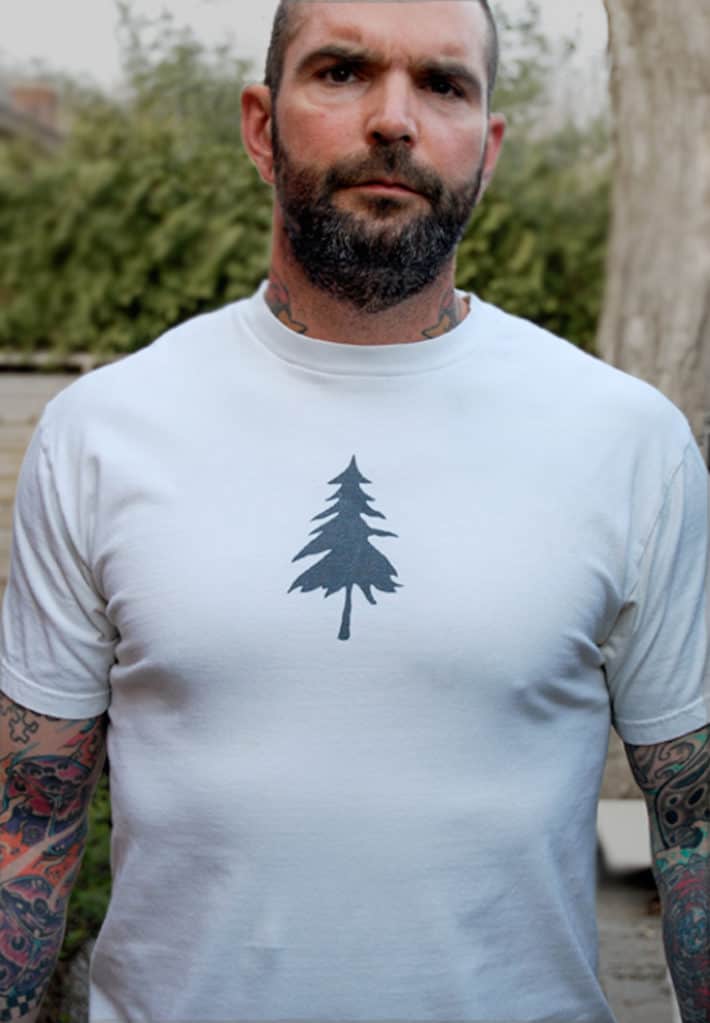 Tattooed man wearing a white tee shirt with the silhouette of a pine tree on it.