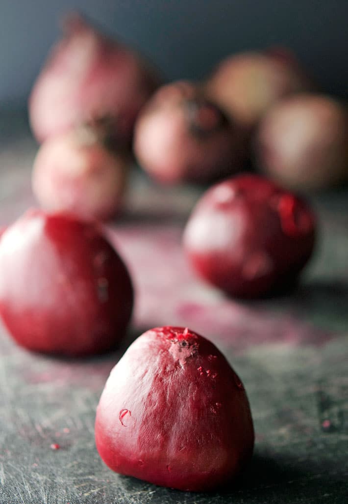 Cooked beets with the skins removed on a black cutting board.