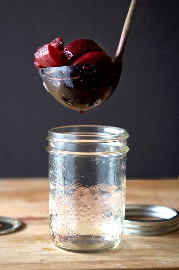 A ladle made out of bamboo lowering pickled beets into a wide mouth mason jar.