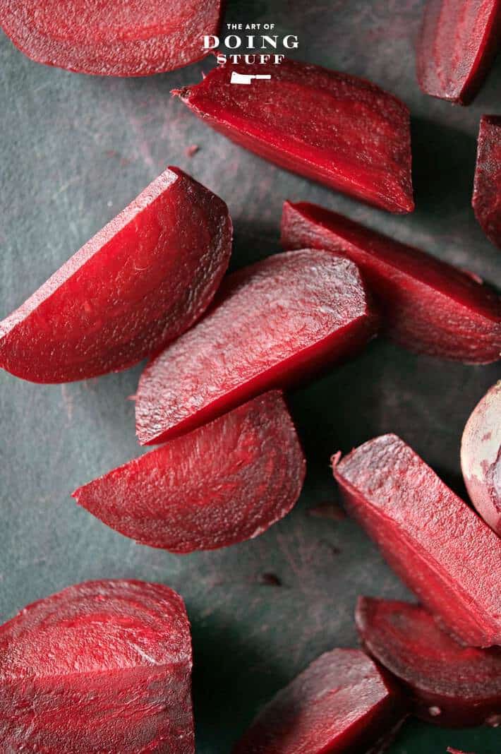 Chopped dark red beets on a black background with sun shining on them.