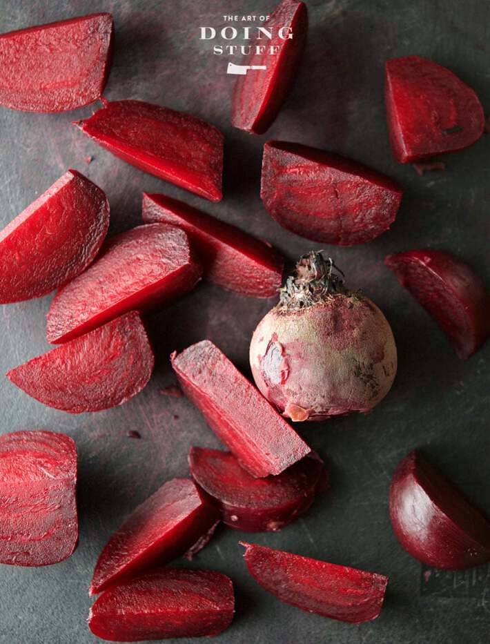 Looking down on a scarred black cutting board covered in chopped beets and one whole beet with the skin on.