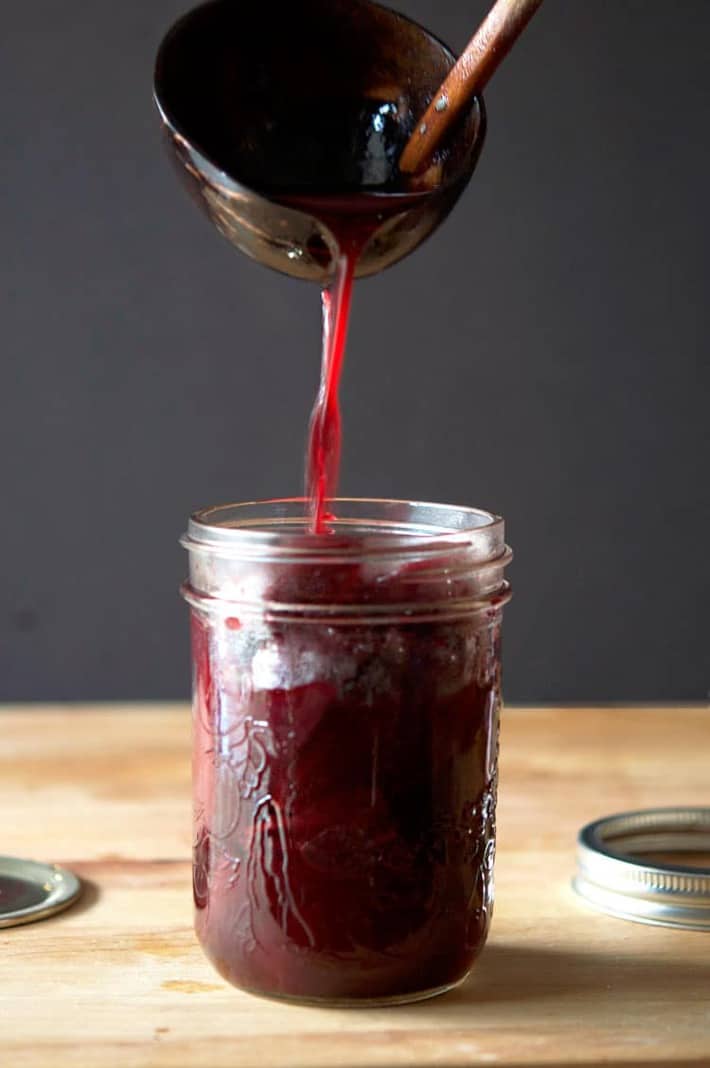 Bamboo ladle pouring dark red brine into a jar of pickled beets.