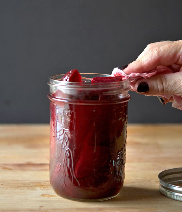 Cleaning the rim of a mason jar filled with newly pickled beets.
