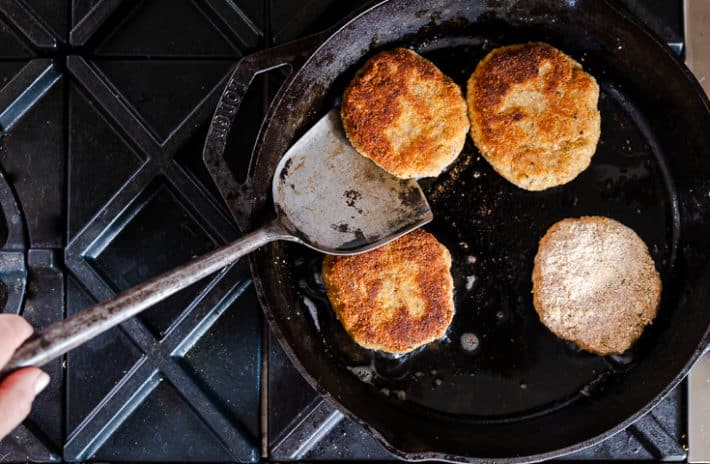 Golden brown chicken burgers pan frying in a cast iron skillet.