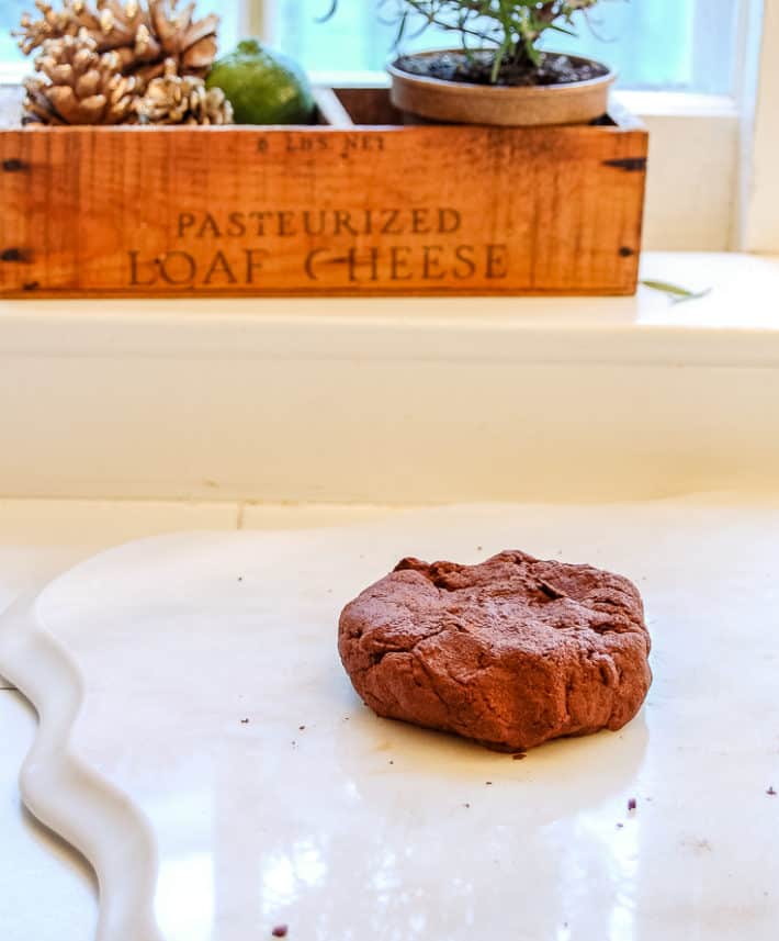 A ball of reddish brown dough sits on a marble cutting board with an antique wood cheesebox in the background.