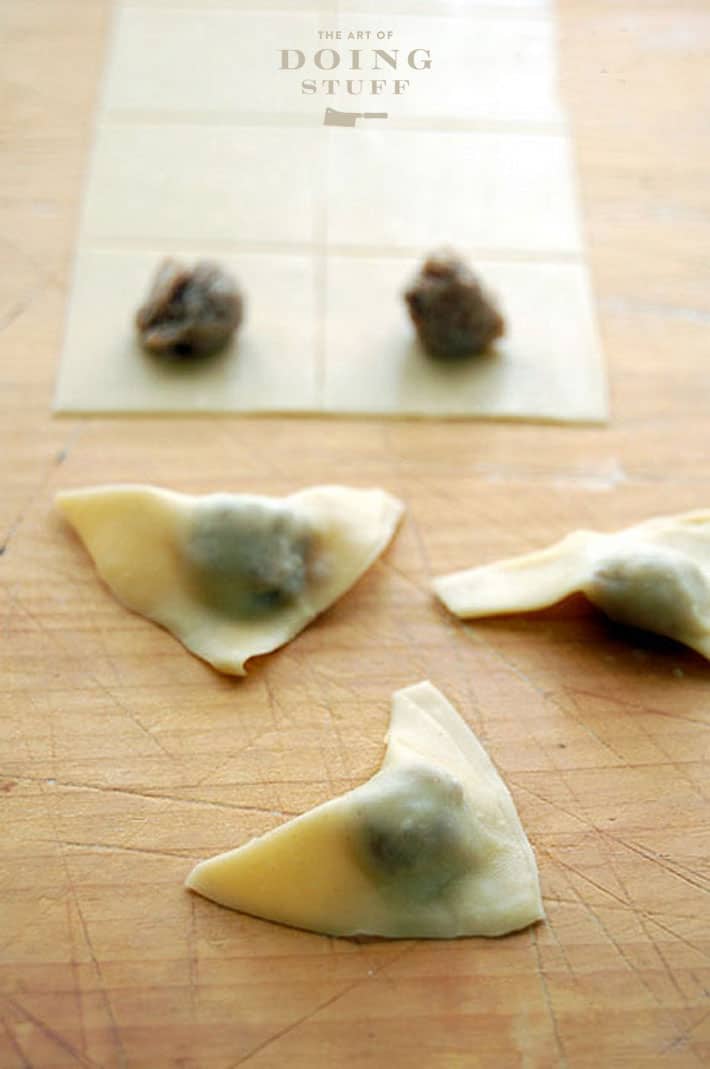 Shaping tortellini into triangles on wood board.