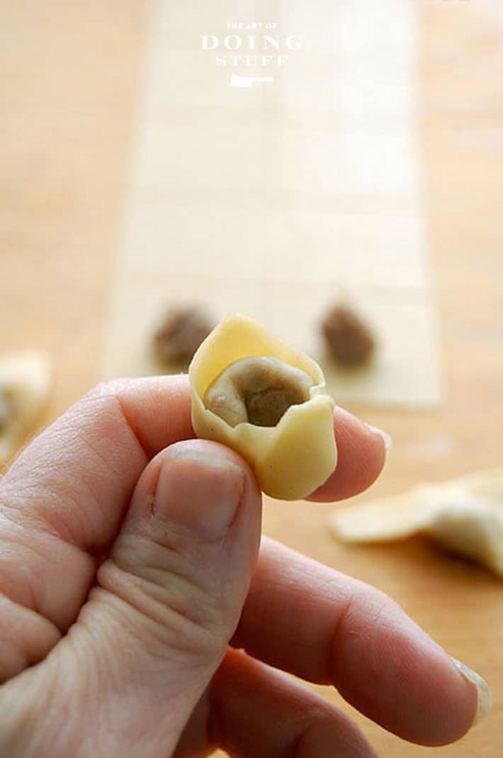 Perfectly formed homemade tortellini held between a thumb and index finger.