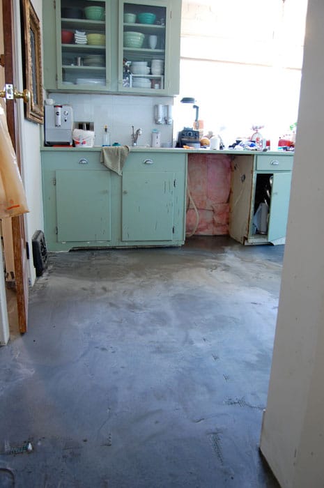 A 1940's kitchen with green cupboards in mid renovation with newly poured self leveling concrete flooring.