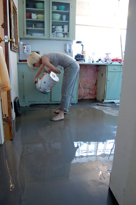 DIYer Karen Bertelsen pouring self leveling concrete over newly installed heated floors in her kitchen.