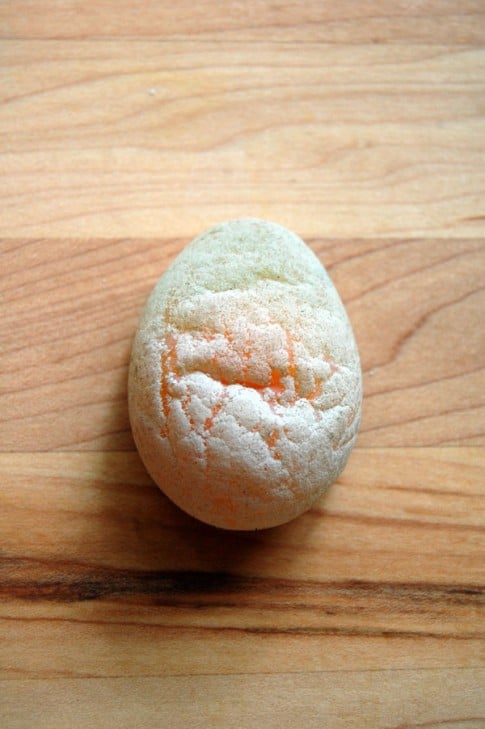 An egg with no shell on a butcher-block counter. The yellow yolk of the egg can be seen through the soft, white membrane. 