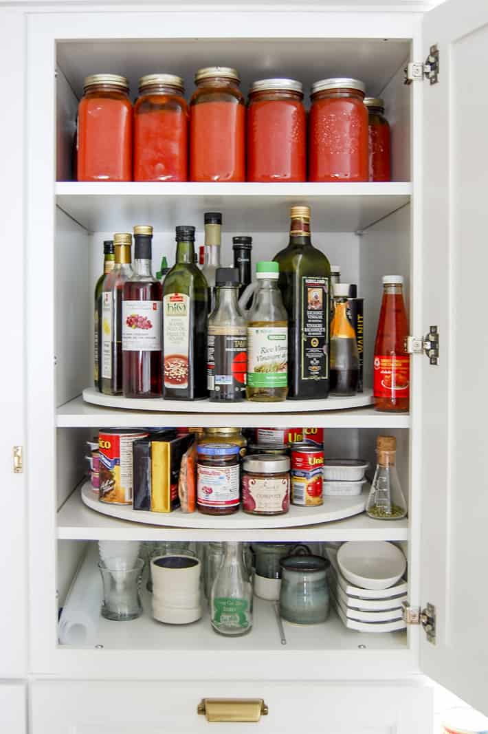 White Martha Stewart pantry cupboard opened to reveal shelves with lazy susans filled with canned and bottled goods.