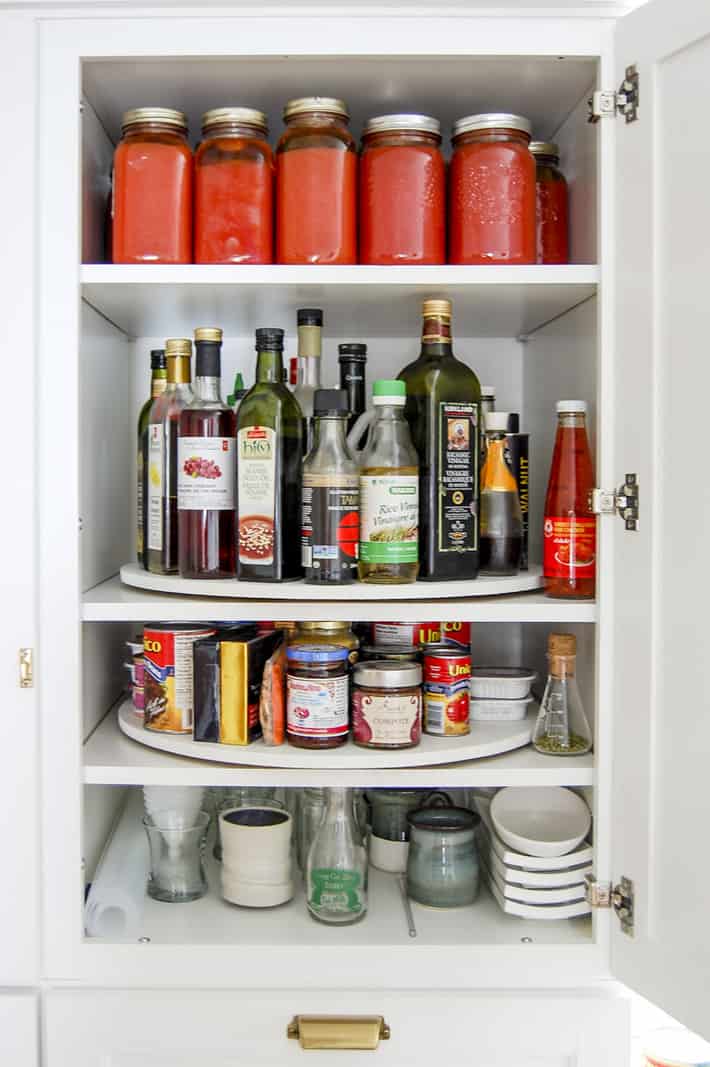 How to DIY a custom Lazy Susan for your cupboards. White Martha Stewart pantry cupboard opened to reveal shelves with lazy susans filled with canned and bottled goods.