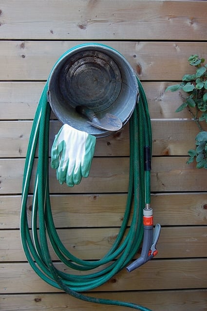 Hose wrapped around bucket screwed to fence.