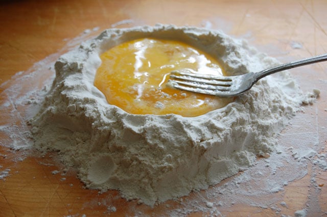 Eggs in the well of a mound of flour being mixed with a fork.