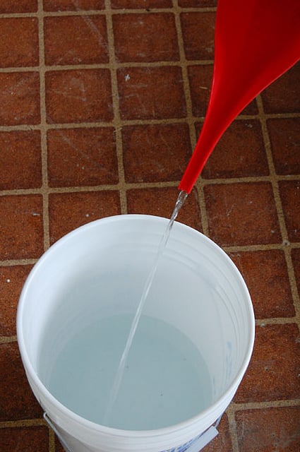 Pouring water into a standard white 5 gallon bucket.