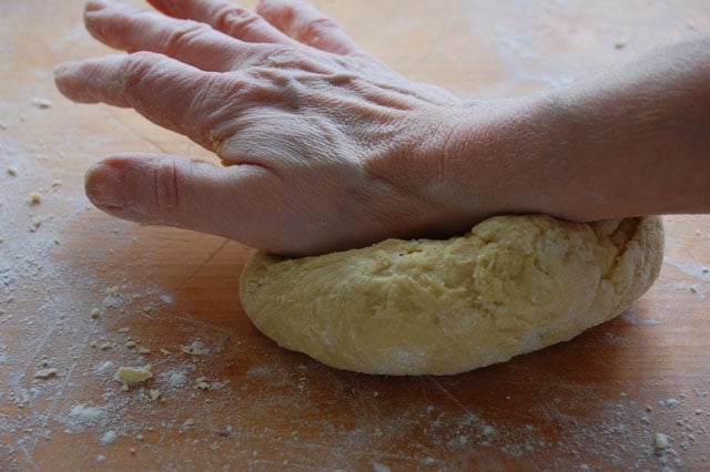 Kneading a ball of homemade pasta on a wood countertop.