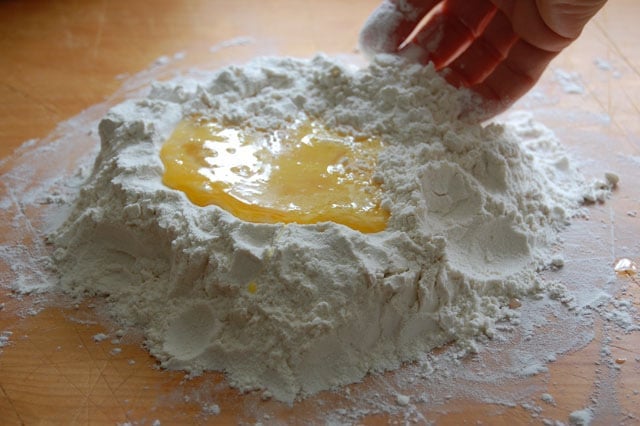 Mixing of flour into eggs with fingers for homemade pasta dough.