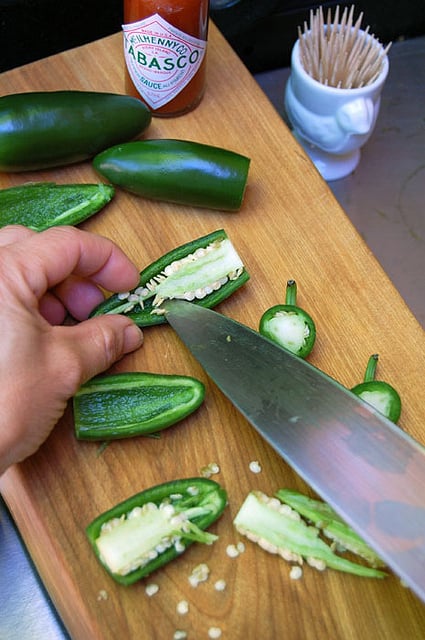 Jalapeño peppers being sliced and deseeded on a wood cutting board.
