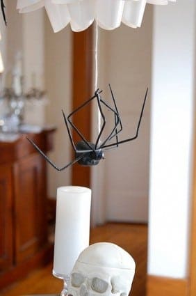 A large fake spider hangs upside down on a thin thread from a chandelier.