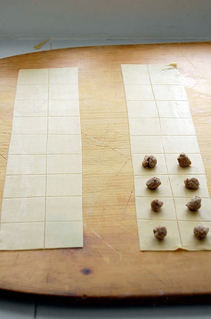 Strips of homemade pasta cut into squares with a ¼ teaspoon of tortellini filling on top.