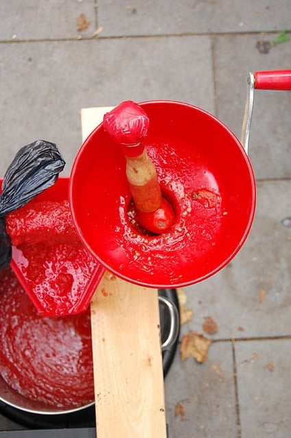 Overhead shot of tomatoes being pushed into the funnel of a manual tomato shot