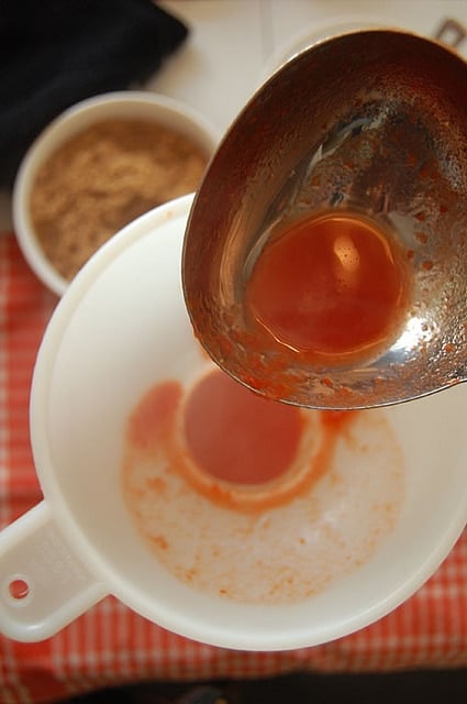 Stainless steel ladle dripping tomato sauce into white funnel over jar.