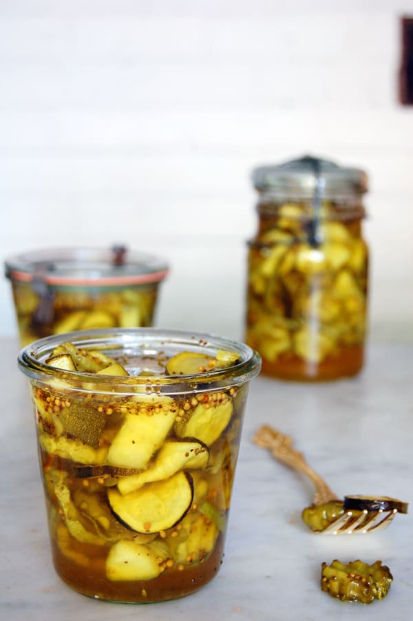 Delicious looking bread and butter pickles in a Wecks jar sitting on a marble counter with antique mason jars in the background.