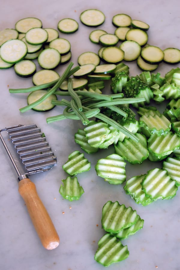 Cucumbers, zucchini and green beans prepped and laying on a marble countertop ready to be made into pickles.