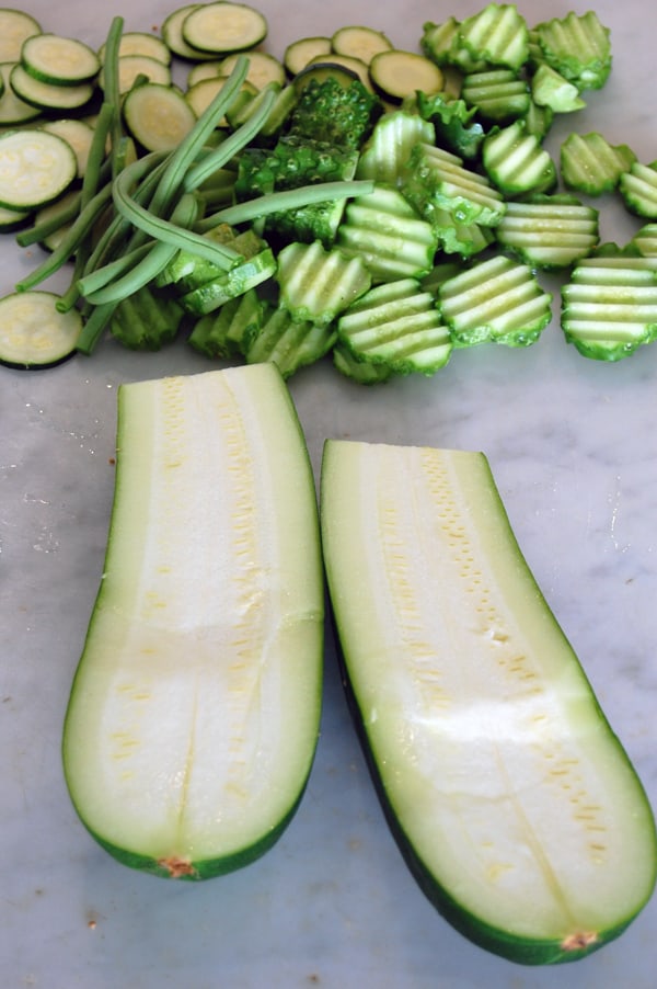 Large zucchini cut in half lengthwise with sliced cucumbers and beans in the background.