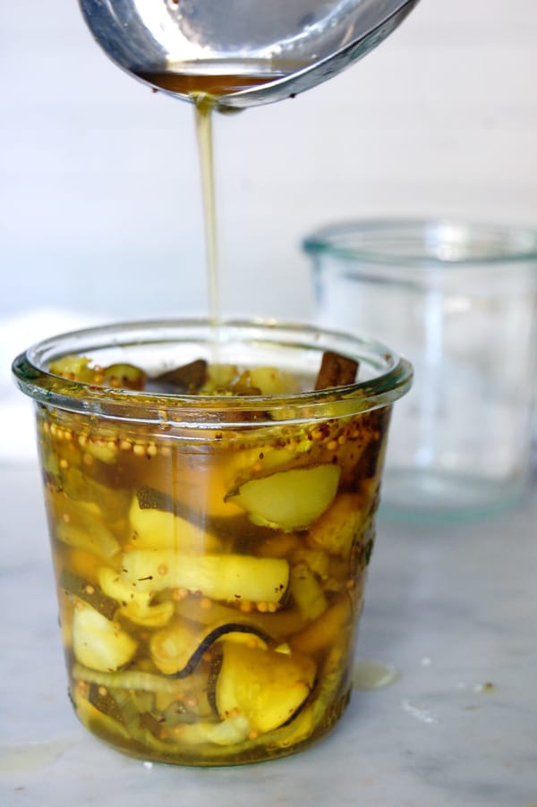 Close up view of turmeric tinged golden brine being poured into a Wecks jar filled with cucumber slices.