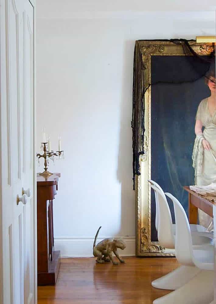 Elegant dining room with Panton S chairs, a lifesized antique portrait draped in black gauze and a mummified cat on the floor.