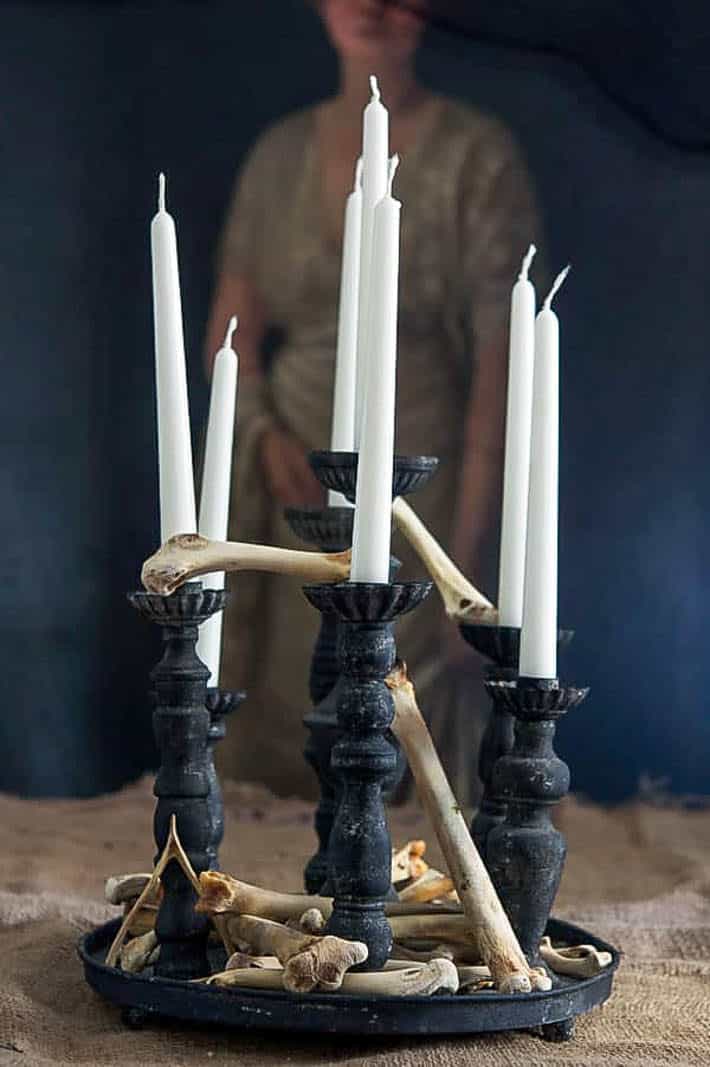 Halloween decoration of a simple black candelabra and white taper candles with bones stacked in between and around the candles.