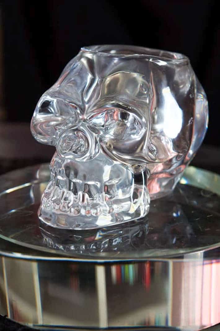 Clear glass skull tea light holder on a round glass riser.