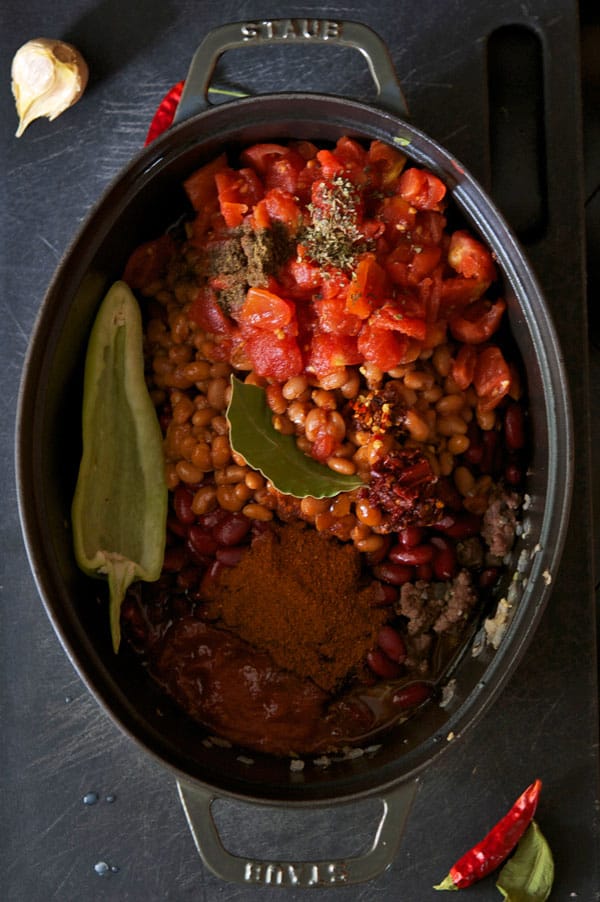 Staub pot filled with ingredients for chili in it including a hot pepper, beans, diced tomatoes and spices.