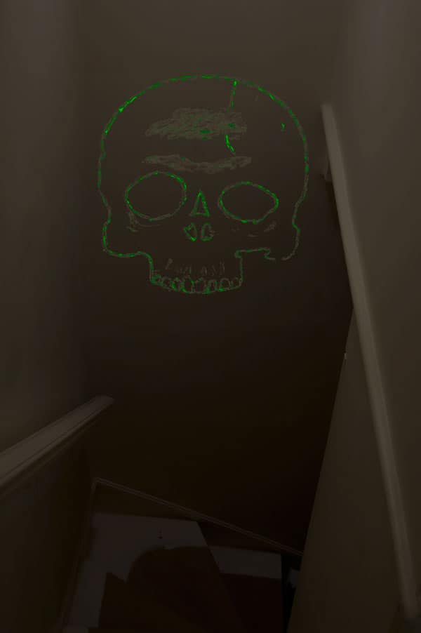 The outline of a skull glows in the dark in a dark staircase.