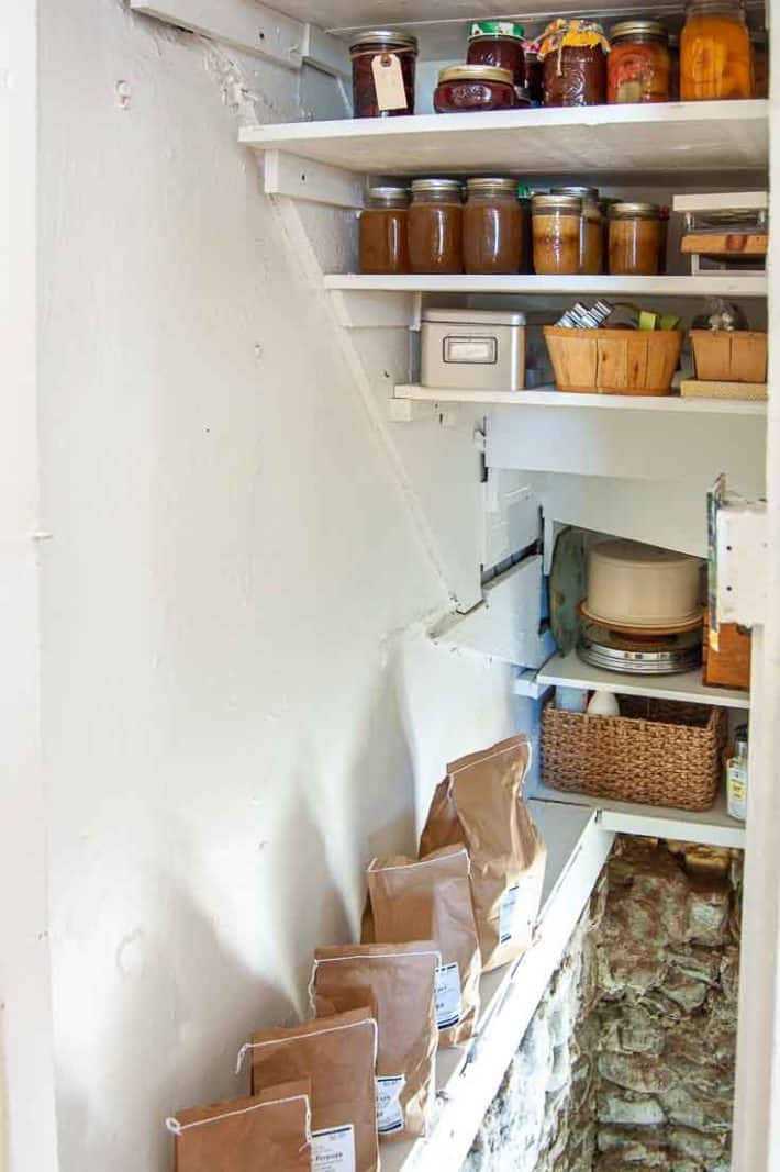 Cleaned up basement stairs with new white shelving filled with preserves and paper bags of seed potatoes lined up on a shelf.