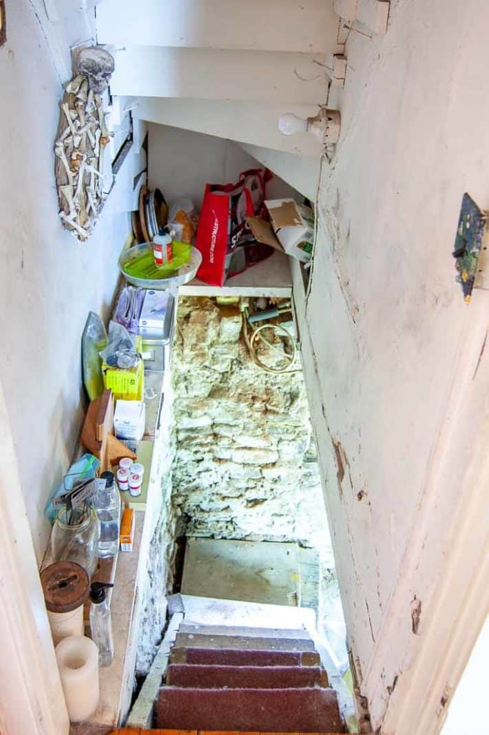 Creepy basement stairs leading down with a cluttered shelf on the side and rubble wall visible at the bottom.