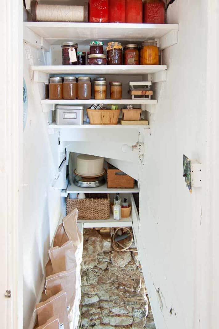 Shelves under stairs providing storage for canned goods and colourful preserves like tomatoes and peaches.