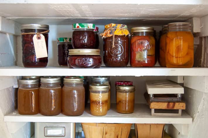 Canned goods lined up on white painted wood under stair shelves.