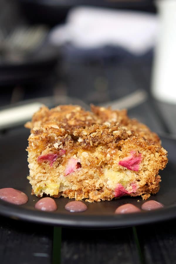 Slice of rhubarb cake on a black plate with dots of coulis.