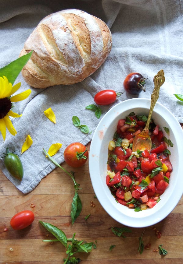Overhead view of an oval ironstone bowl filled with diced tomatoes and basil, sitting alongside a loaf of bread.