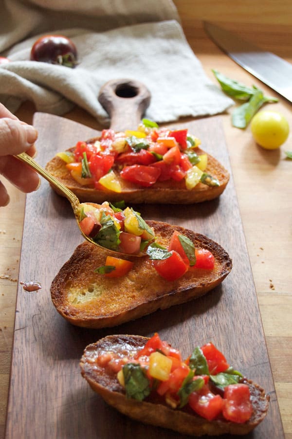 Marinated tomatoes and basil being topped onto olive oil fried bread with a gold spoon.