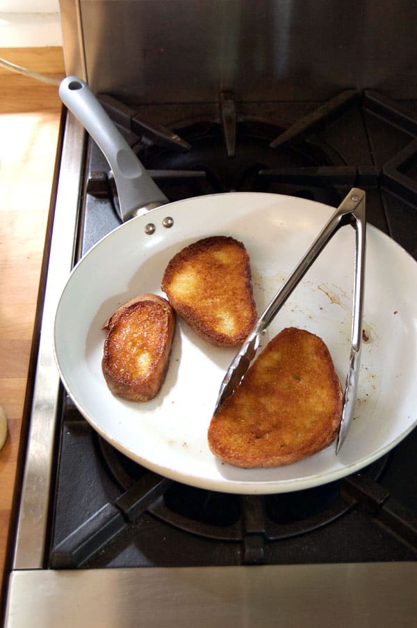 Bread fried to a golden brown in a white non stick pan with olive oil.