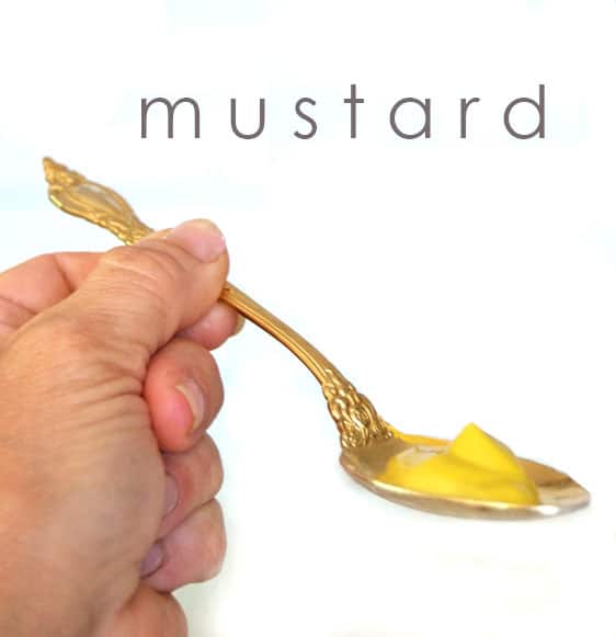 A teaspoon of mustard on a gold plated ornate spoon.