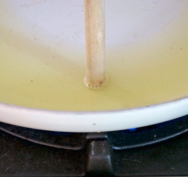 A wooden spoon is touched into hot oil to see if bubbles form around it, proving the oil is hot enough for frying.