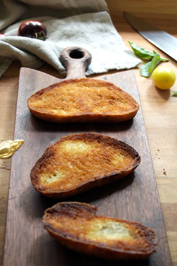 Crunchy rustic bread fried to a golden brown in olive oil sits on a wood cutting board.