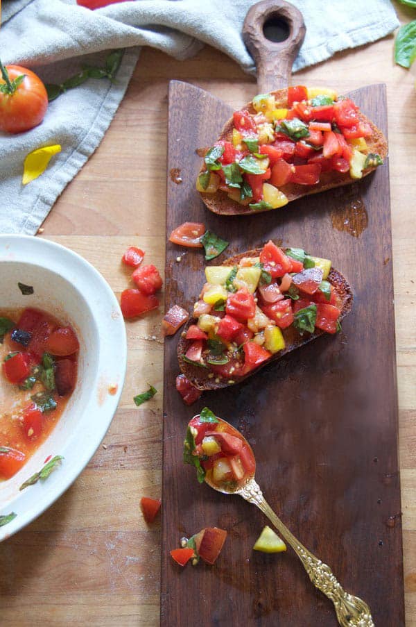 Bruschetta topped fried bread sits on a wood cutting board.