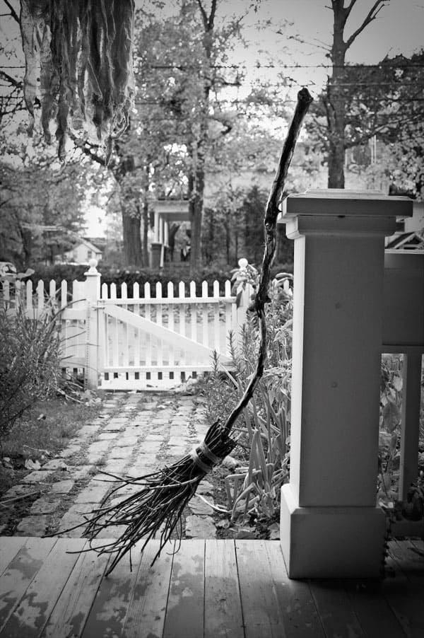 A DIY witches broom made with twigs and branches rests on an old porch.