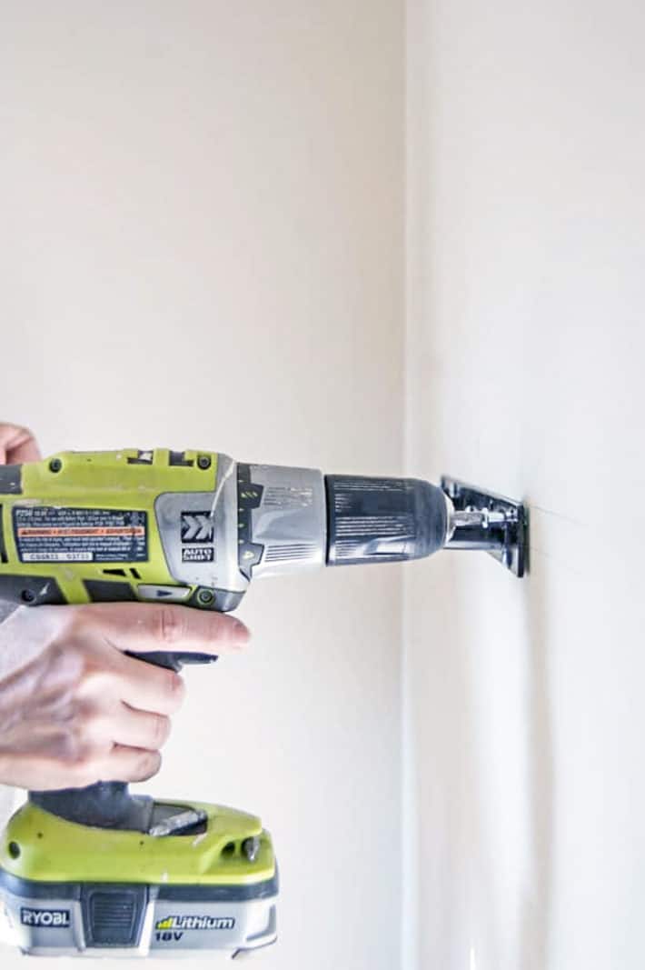 Securing a bracket to a wall using molly bolts and a bright green Ryobi cordless drill.