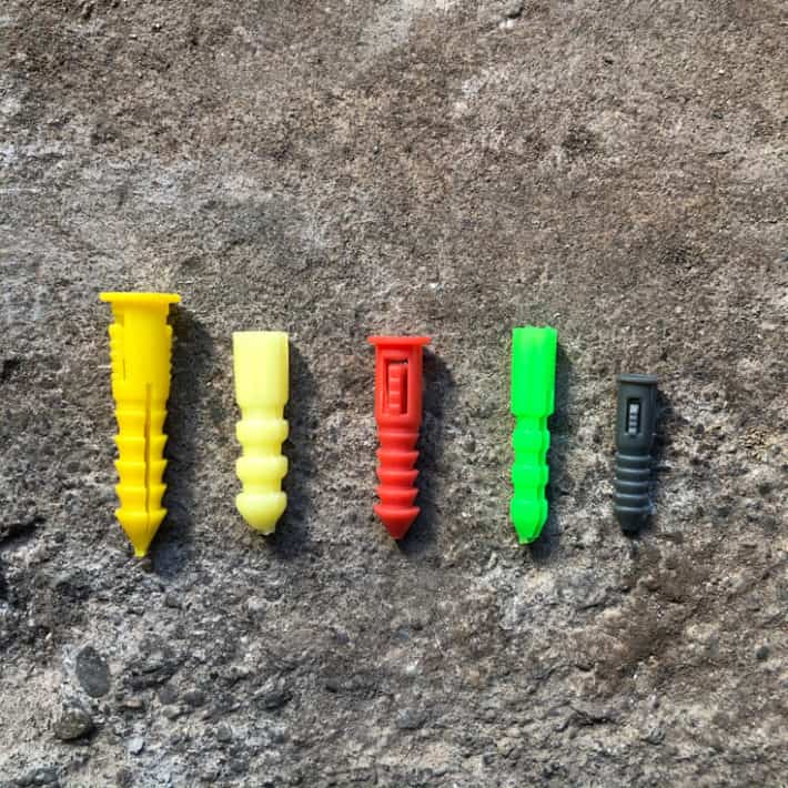 An array of colourful plastic wall anchors laid in a row on concrete.